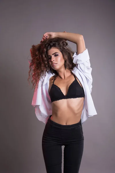 Studio gri bir arka plan üzerinde siyah kıvırcık saçlı oldukça ince kız