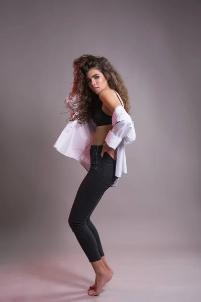 Studio gri bir arka plan üzerinde siyah kıvırcık saçlı oldukça ince kız