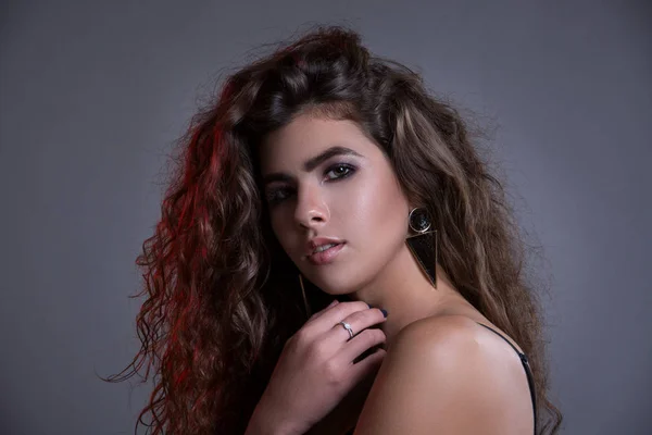 Studio gri bir arka plan üzerinde siyah kıvırcık saçlı oldukça ince kız