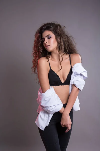 Studio gri bir arka plan üzerinde siyah kıvırcık saçlı oldukça ince kız