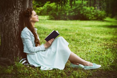 Parkta kitap okuyan güzel genç bir kadın.