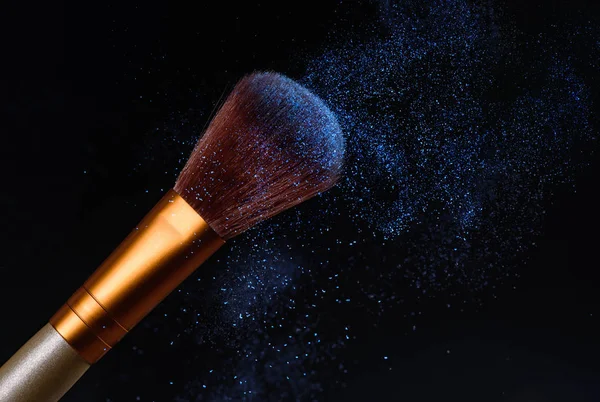 Makeup brush on black background with blue powder