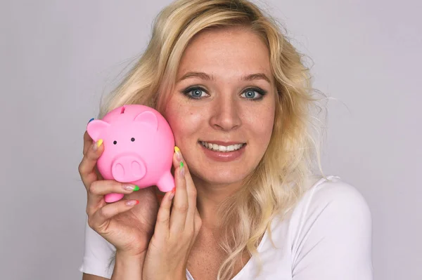 Lächelndes Mädchen mit Sommersprossen hält ein Sparschwein. — Stockfoto