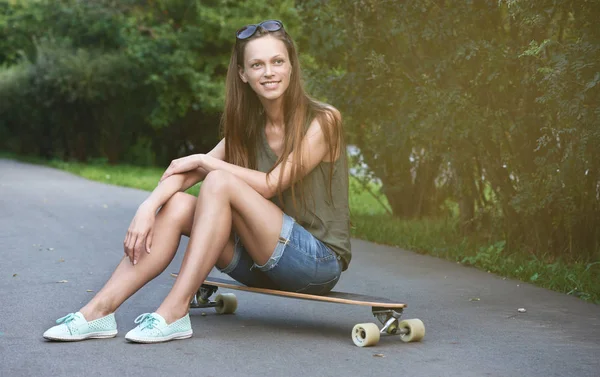 Pretty genç kız longboard üzerinde oturur