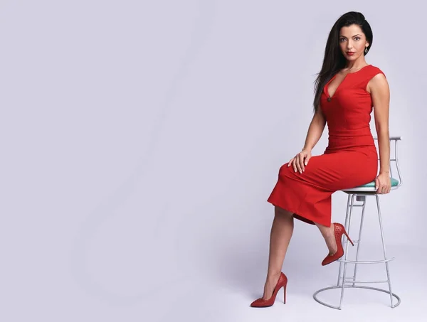 Modische Frau im roten Kleid sitzt auf Stuhl. — Stockfoto