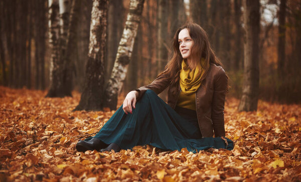 Beautiful woman is sitting on a yellow leaves in the autumn park