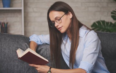 Evindeki kanepede kitap okuyan güzel bir kız.