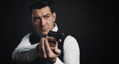 Ciddi bir adam siyah arka planda bir silah tutuyor.