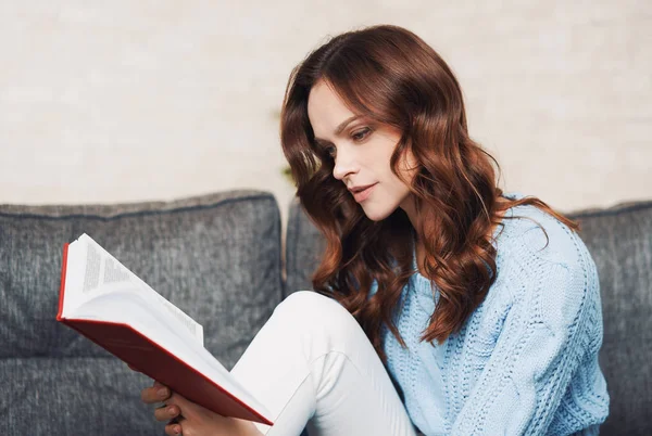 En vacker kvinna läser en bok hemma. — Stockfoto