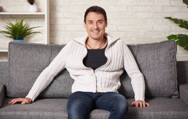 Beyaz kazaklı mutlu adam kanepede oturuyor.