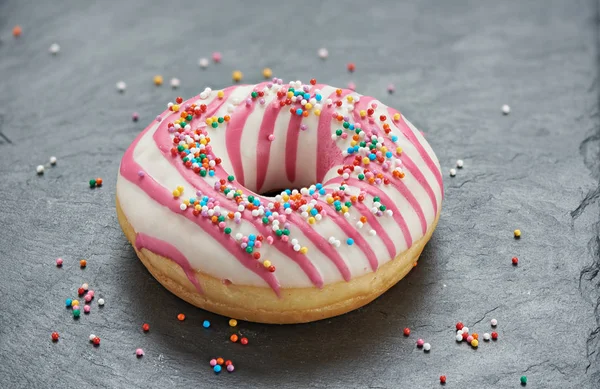 Glazed round donut with sprinkles on a stone table — Stock Photo, Image