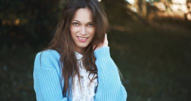 Güzel bir kadın örgü kazak giyiyor ve parkta dinleniyor. Açık hava portresi.