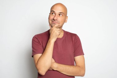 Kel adam düşünüyor, yukarı bakıyor ve gülümsüyor. Gri stüdyo duvarında izole edilmiş.