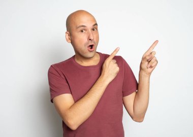 Şaşırmış kel adam, gri stüdyo duvarında izole edilmiş kopyalama alanını işaret ediyor.