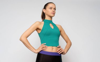 Atletik vücutlu güzel bir kadın gri arka planda izole edilmiş spor giysiler giyiyor.
