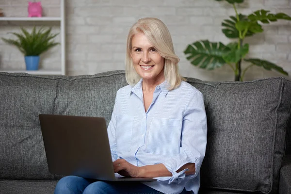 Šťastná Blondýna Senior Žena Pracuje Notebookem Zatímco Sedí Pohovce Doma — Stock fotografie