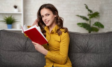 Kız kanepede oturur ve evde kitap okur.