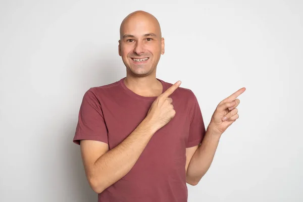 一个穿着红色T恤的快乐秃头男子的画像 手指指向灰色背景之外的复制空间 — 图库照片