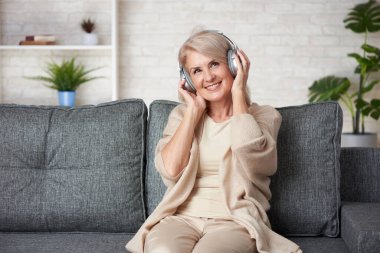 Kaygısız son sınıf öğrencisi kadın evde bir kanepede otururken müzik dinliyor..
