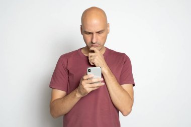 Kırk yaşında kel bir adam, beyaz telefondan haber okuyor.