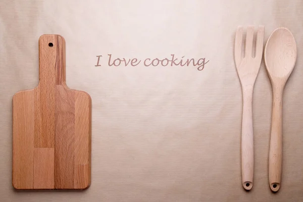 Cutting board and wooden spoons on Kraft background with the wor