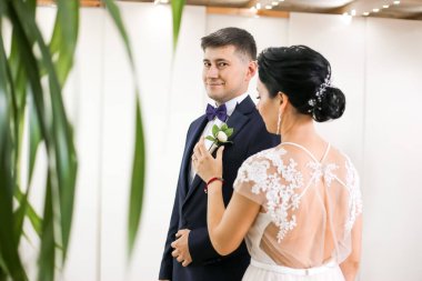 Şık bir elbise içinde gelin ve arka planda bir takım elbise içinde damat