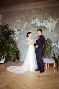 Şık bir elbise içinde gelin ve arka planda bir takım elbise içinde damat