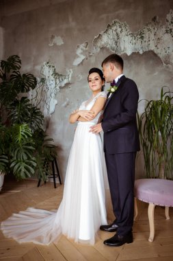 Şık bir elbise içinde gelin ve arka planda bir takım elbise içinde damat