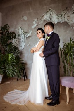 Şık bir elbise içinde gelin ve arka planda bir takım elbise içinde damat