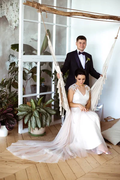 Hermosa novia en un vestido elegante se sienta en una hamaca de macramé un — Foto de Stock