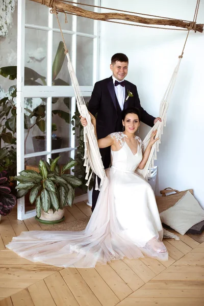 Hermosa novia en un vestido elegante se sienta en una hamaca de macramé un — Foto de Stock