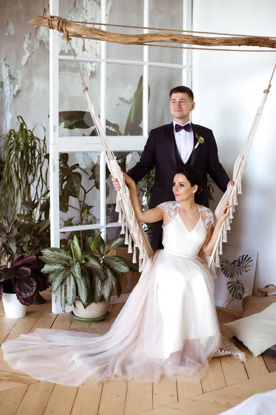 Hermosa novia en un vestido elegante se sienta en una hamaca de macramé un — Foto de Stock