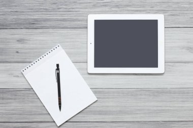 Tablet ve boş bir defter, tahta bir arka planda bir masanın üzerinde duruyor.