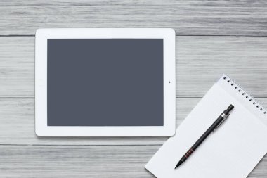 Tablet ve boş bir defter, tahta bir arka planda bir masanın üzerinde duruyor.