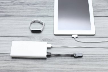 Tablet ve takip cihazı tahtadan yapılmış arka plandaki bir güç bankasından şarj ediliyor.