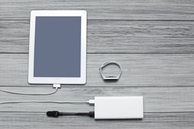 Tablet ve takip cihazı tahtadan yapılmış arka plandaki bir güç bankasından şarj ediliyor.