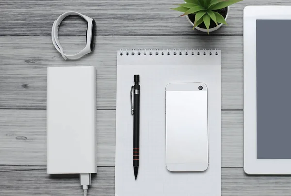 Tablet, blank notebook, phone and charger on the background of wooden boards