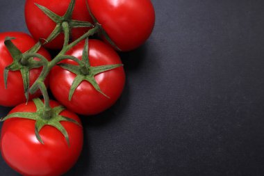 Dal üstünde kırmızı domatesler. Siyah desenli arka planda sebzeler.