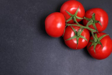 Dal üstünde kırmızı domatesler. Siyah desenli arka planda sebzeler.