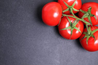 Dal üstünde kırmızı domatesler. Siyah desenli arka planda sebzeler.