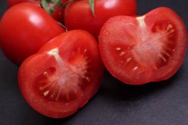 Dal üstünde kırmızı domatesler. Siyah desenli arka planda sebzeler.