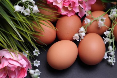 Siyah desenli arka planda bahar çiçekleri arasında paskalya yumurtaları.