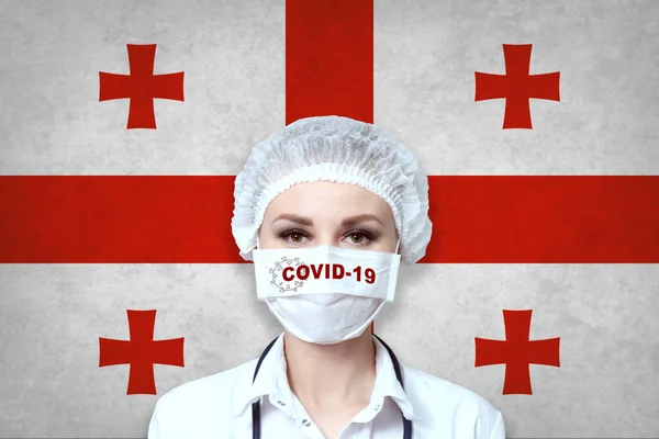 戴医疗面罩的女医生 在格鲁吉亚国旗模糊的背景上刻有Covid 19字样 大流行性病毒Covid 保健和医疗概念 — 图库照片
