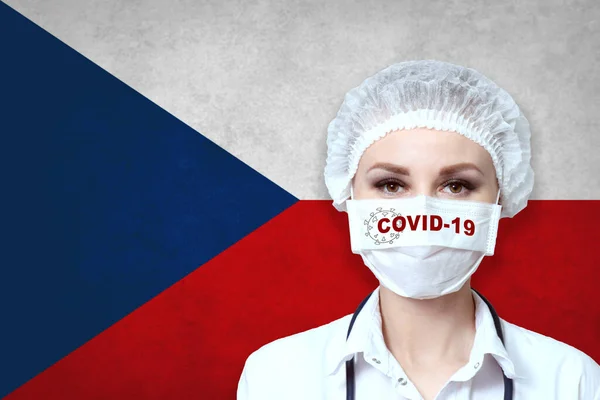 戴医疗面罩的女医生 在捷克共和国国旗模糊的背景上刻有Covid 19字样 大流行性病毒Covid 保健和医疗概念 — 图库照片