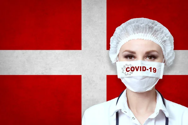 Female doctor in medical mask with the inscription COVID-19 on a blurred background of the flag of Switzerland. Pandemic virus COVID-19. Healthcare and medical concept.