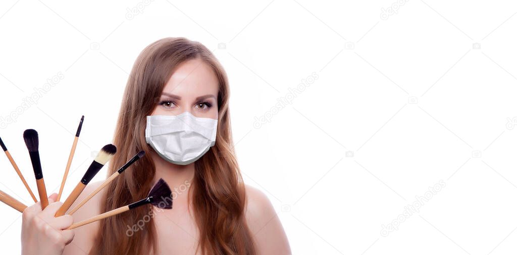 Beautiful young woman with long hair in a medical mask holding a makeup brush.