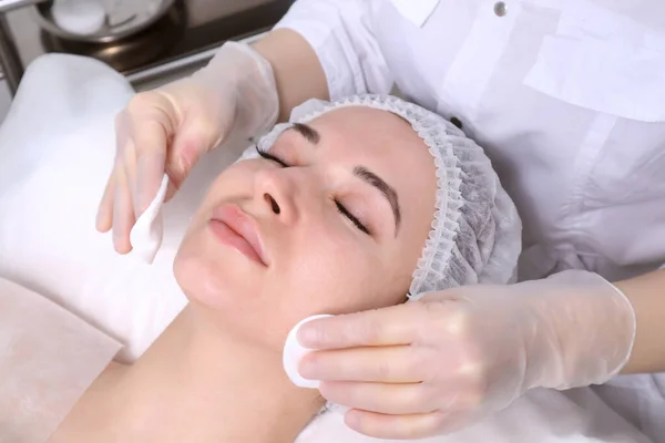 Beautician makes the cleansing procedure a young beautiful girl patient. The concept of skin care face and body