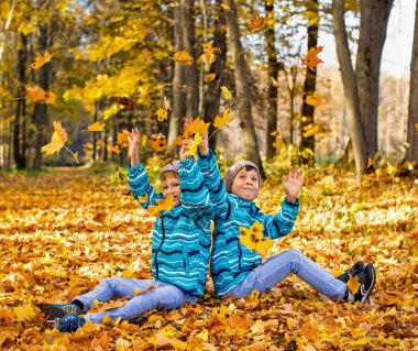 Twin boys in the park under falling maple leaves. Autumn.
