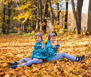 Twin boys in the park under falling maple leaves. Autumn.