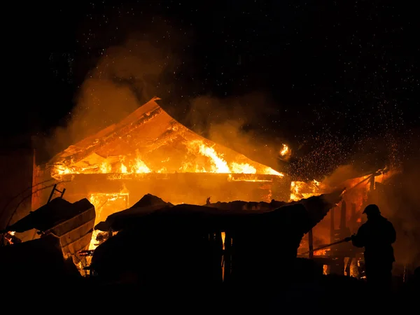 Firefighter at burning fire flame on wooden house roof — Stock Photo, Image